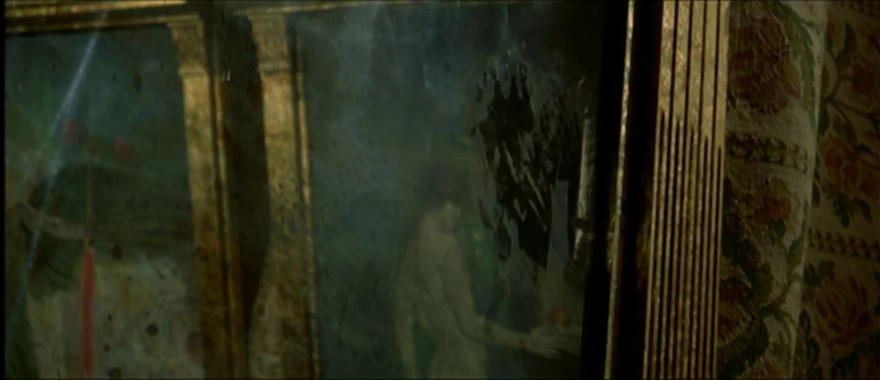 Flesh For Frankenstein (1973) movie still: closeup — A tarnished gilt mirror frame is covered in grime and smudge marks. The glass surface reflects…