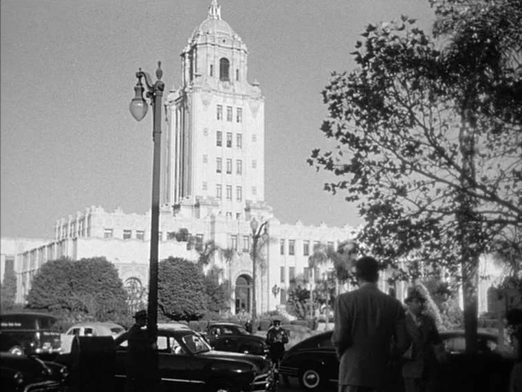 In a Lonely Place (1950) movie still: establishing — A historic municipal building with a central clock tower stands behind a busy street. People…
