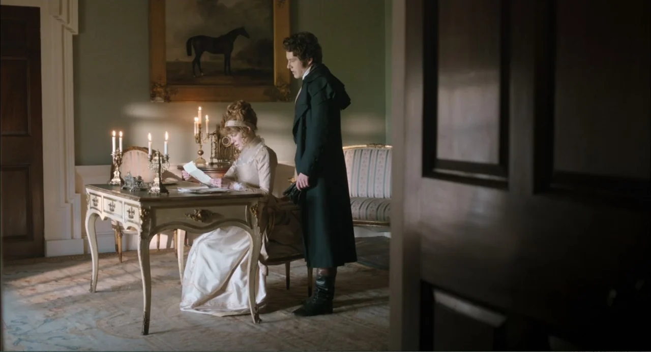 Love & Friendship (2016) movie still: fullbody — A 19th-century room contains an ornate writing desk and a large horse portrait painting. A seated…