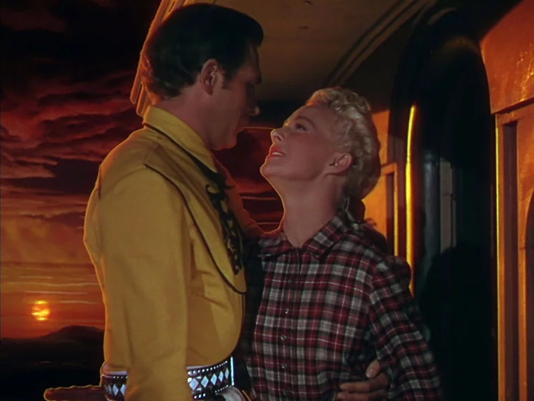 Annie Get Your Gun (1950) movie still: medium — A man and a woman stand together on a porch in front of a backdrop. The background displays a…