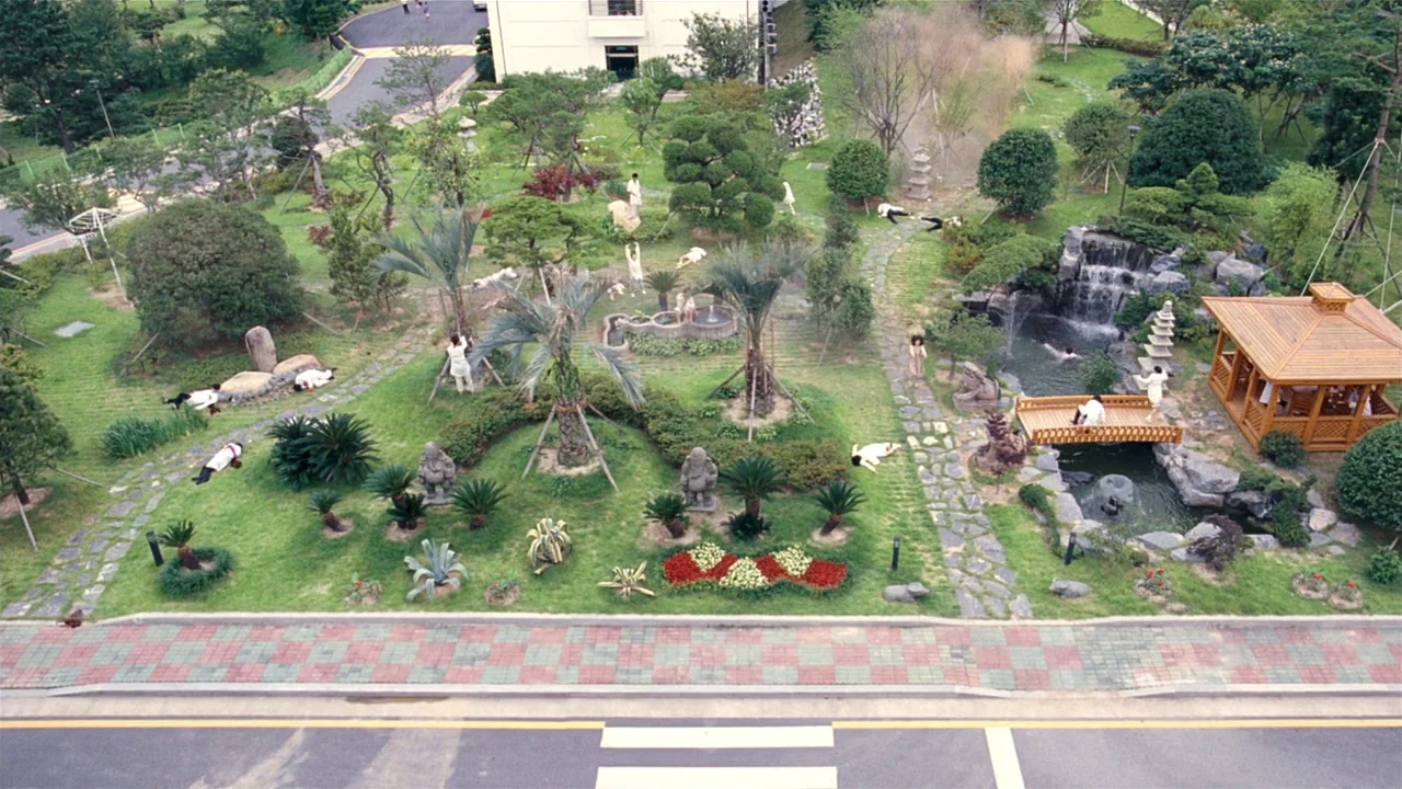 I’m A Cyborg, But That’s Okay (2006) movie still: establishing — A manicured public park features stone pathways, a small waterfall, and a wooden…