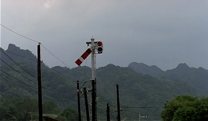 Dust In The Wind (1986) movie still: wide — An outdoor railway signal stands before a backdrop of hazy, tree-covered mountain ranges. The overcast…