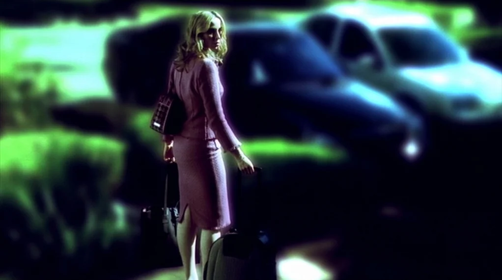 Broken Flowers movie still: fullbody — A parking lot at night is obscured by deep shadows and high-contrast green light. A woman in a pink suit…