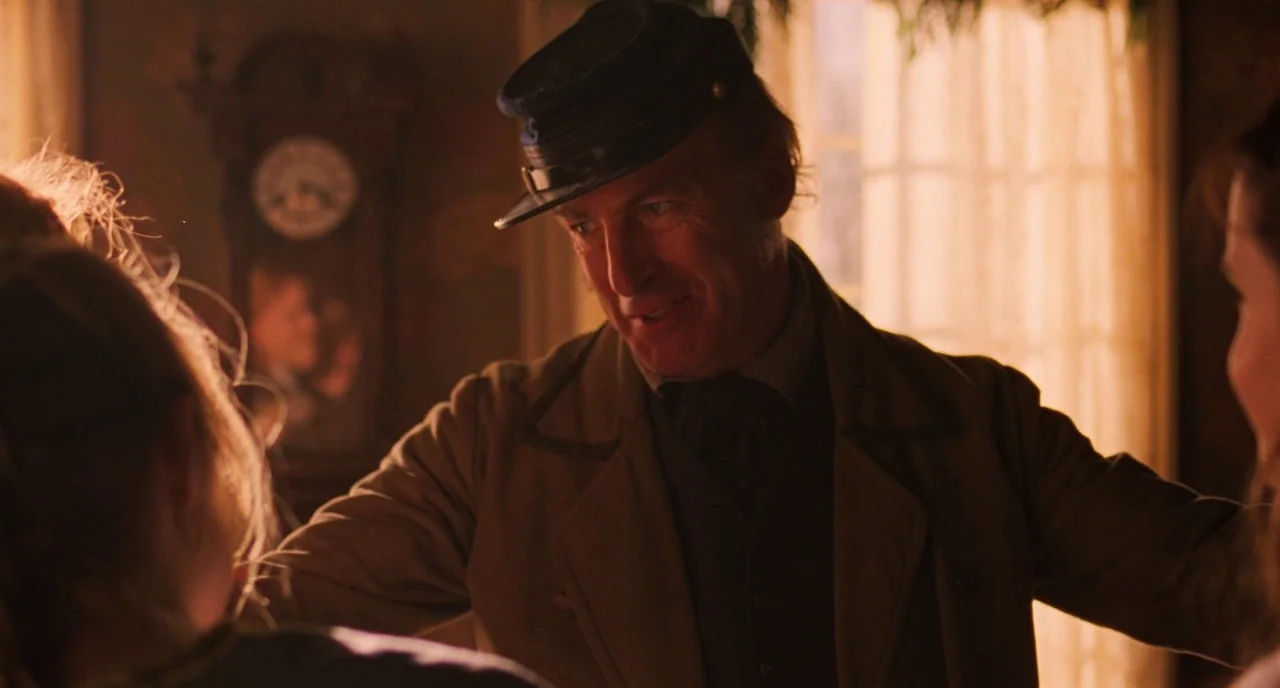 Little Women (2019) movie still: medium — A dimly lit nineteenth-century parlor contains a grandfather clock and draped windows. A man wearing a…