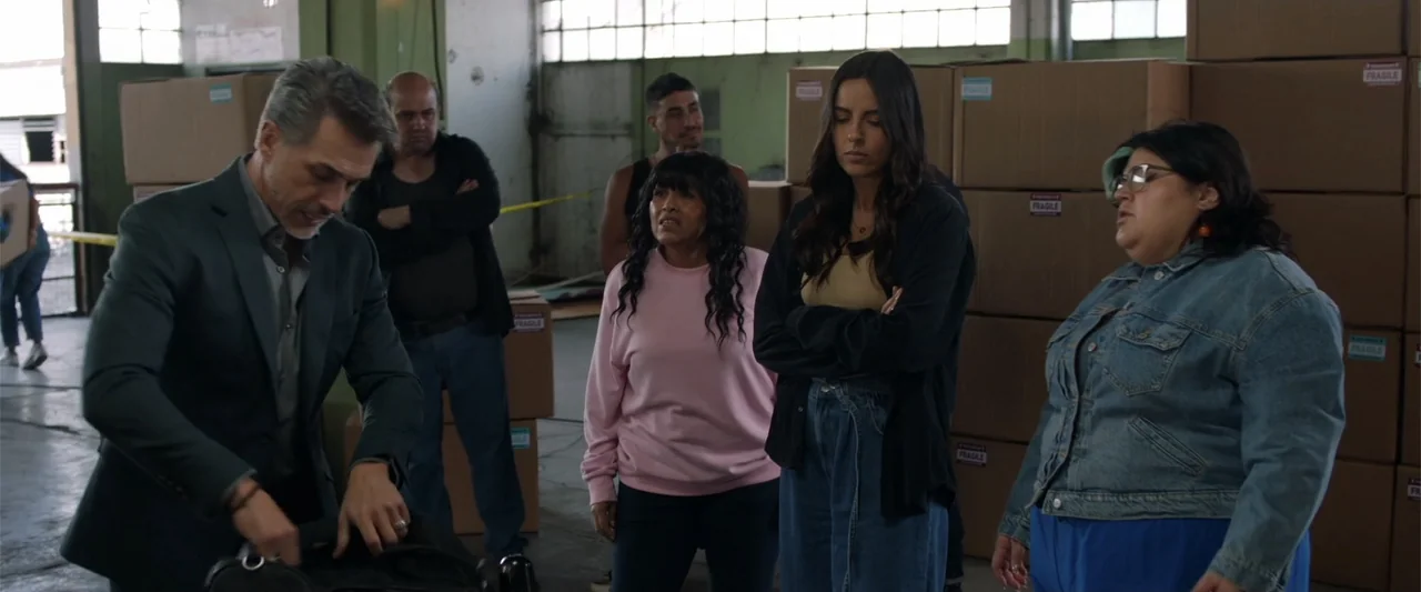 Winner Takes the Cake (2025) movie still: medium — An industrial storage area contains stacked cardboard boxes and a concrete floor. Five…