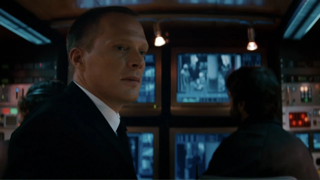The Tourist (2010) movie still: medium — A dark surveillance room contains multiple glowing computer monitors and metallic technical consoles. A man…