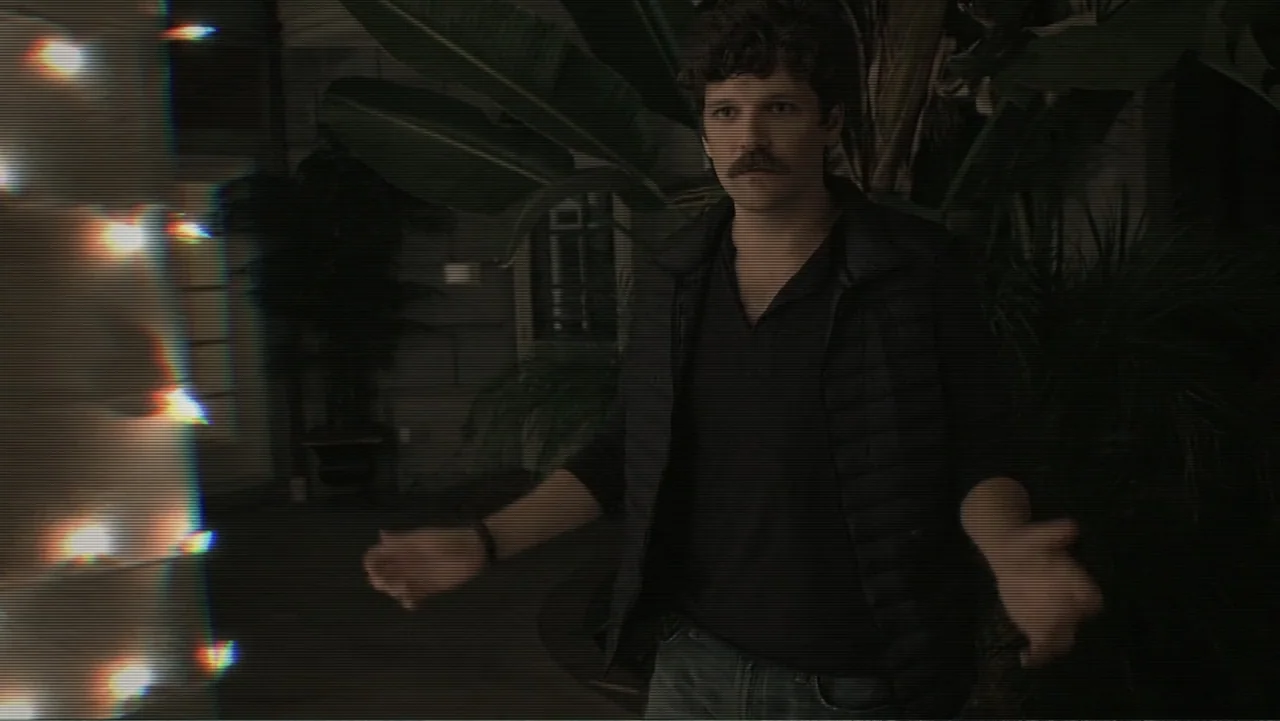 Paranormal Activity: The Ghost Dimension (2015) movie still: medium — A man stands outdoors at night in front of large tropical potted plants. He…