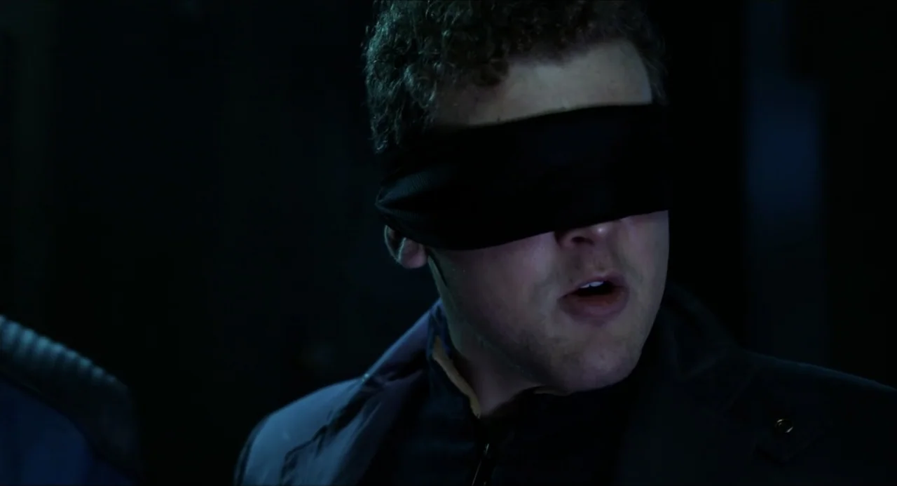 Henry Danger: The Movie (2025) movie still: closeup — A dark, underexposed interior space surrounds the man. He wears a black blindfold over his…