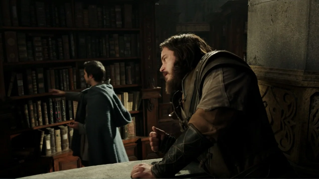 Warcraft (2016) movie still: medium — A dark stone library with towering wooden bookshelves filled with numerous old books. A bearded man in armor…