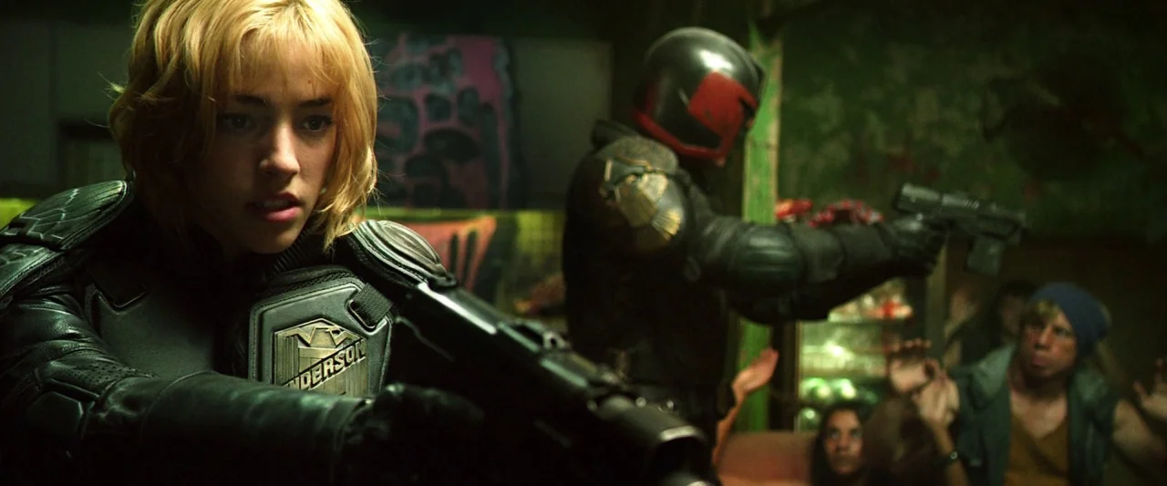Dredd (2012) movie still: medium — A dimly lit room with distressed walls and visible graffiti marks the interior space. Two armored law enforcement…