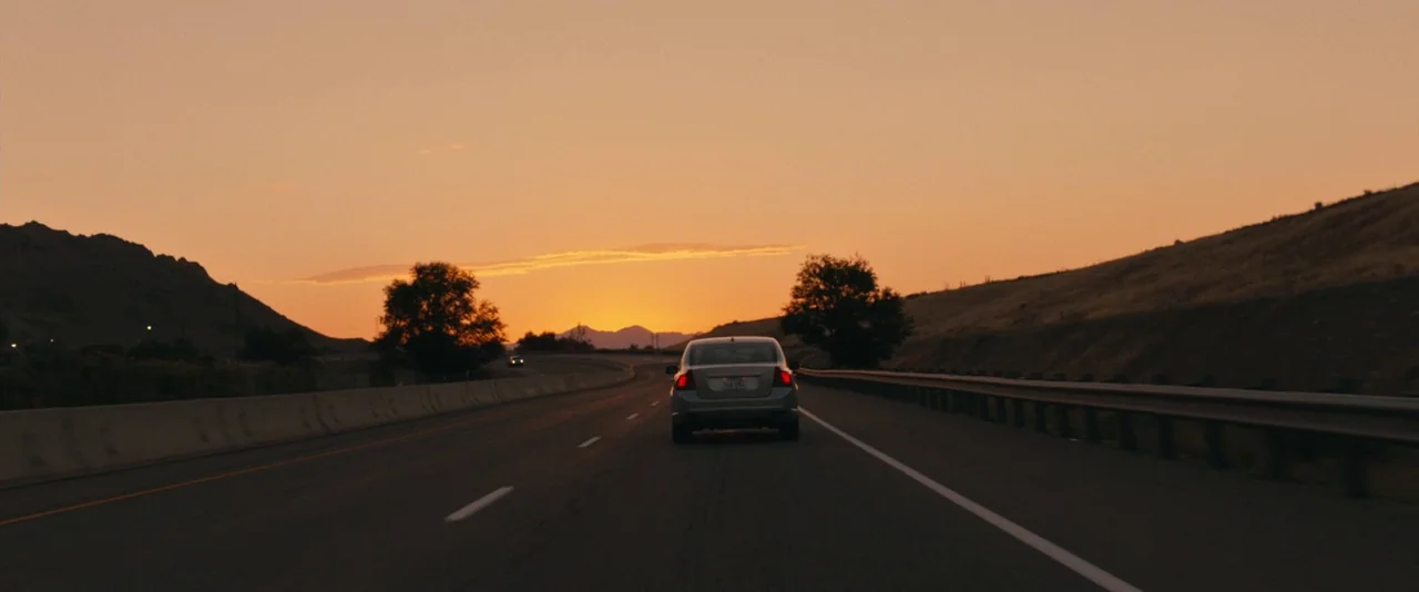 Brigsby Bear (2017) movie still: wide — An asphalt highway stretches into the distance toward a low mountain range at sunset. A lone silver car…