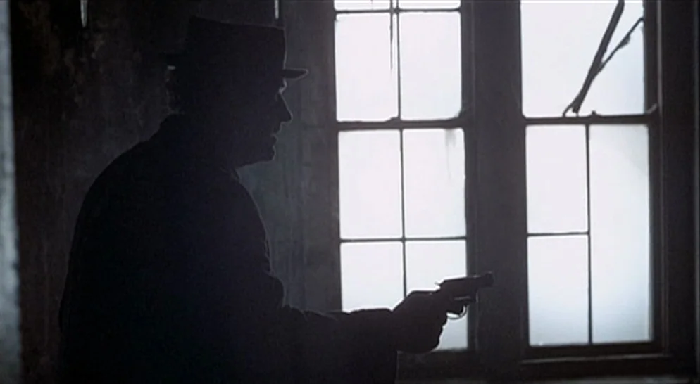 The French Connection (1971) movie still: medium — A dimly lit room with peeling paint features a large multi-pane glass window. A man in a hat…
