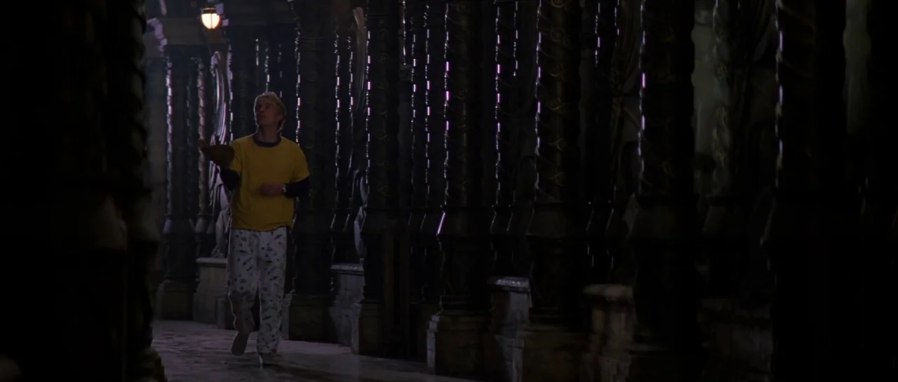 The Haunting (1999) movie still: fullbody — A long stone corridor features rows of carved cylindrical pillars disappearing into darkness. A teenage…