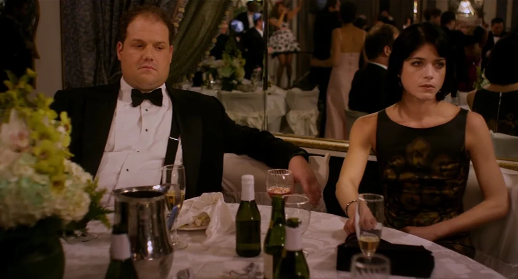 Dark Horse (2011) movie still: medium — A man and a woman sit at a round table covered in white linen. The background shows a crowded ballroom with…