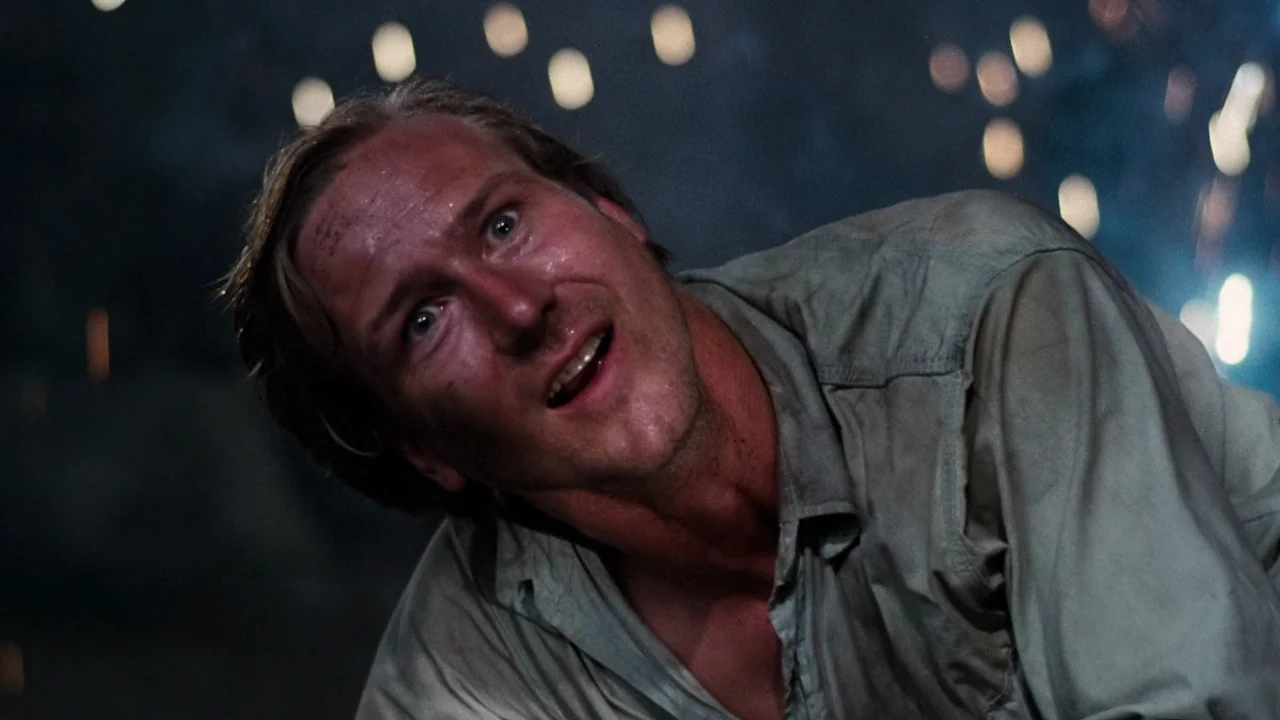 Altered States (1980) movie still: closeup — A dark subterranean space filled with floating sparks and shadows. A man lies on the ground, face…