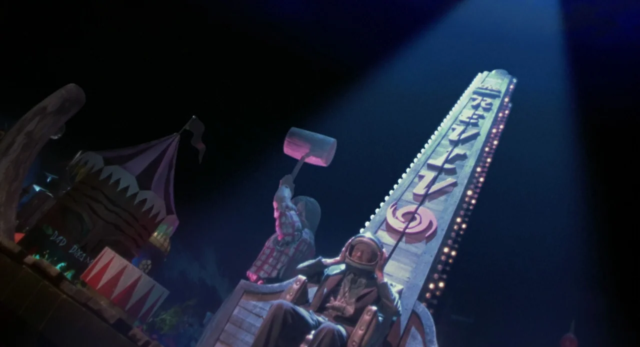 Monkeybone (2001) movie still: wide — A night time carnival attraction features a towering test-your-strength sign with neon lighting. A man in a…