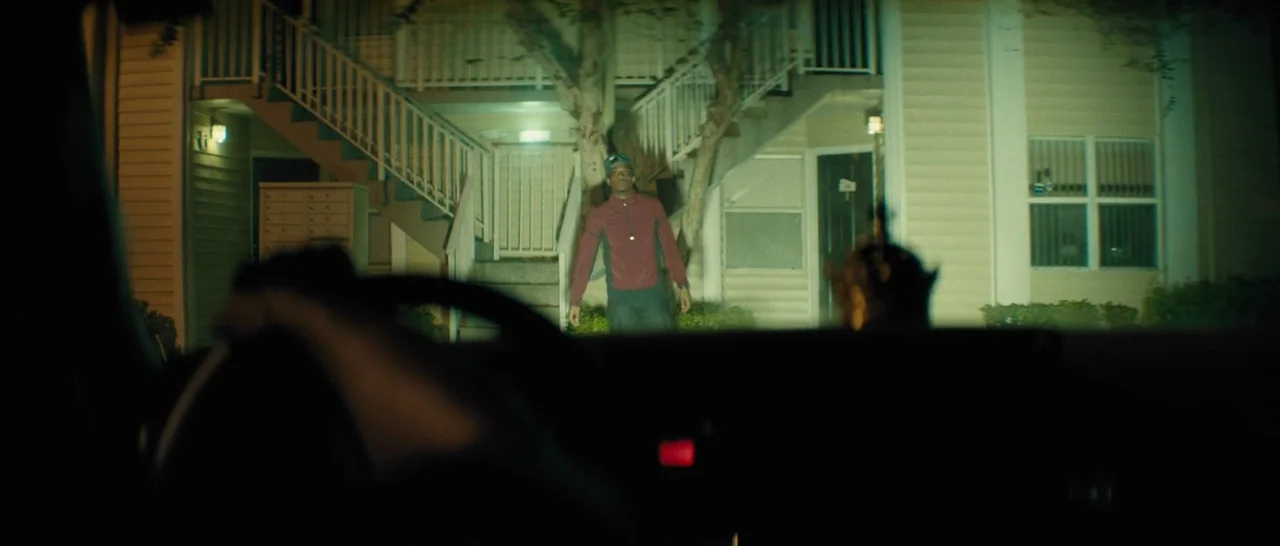 Moonlight (2016) movie still: wide — A dark apartment complex exterior at night with a staircase and concrete walkways. A young man stands in the…