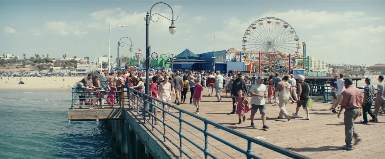 Pacific Rim: Uprising (2018) movie still: wide — A sunny day on a wooden amusement pier packed with many diverse pedestrians. A large ferris wheel…