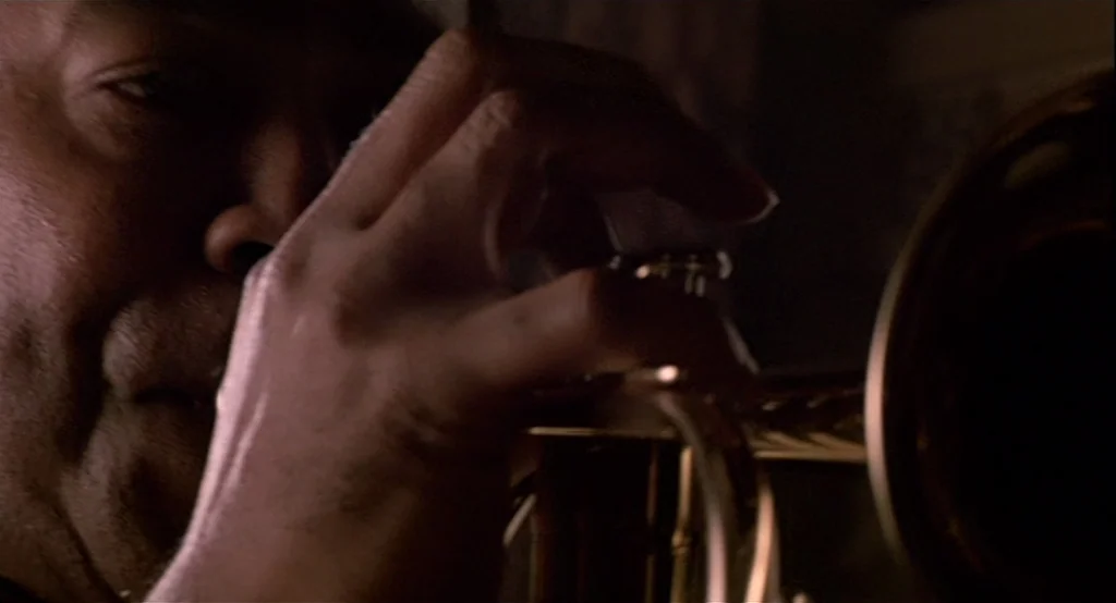 The Cotton Club (1984) movie still: closeup — A man's face and hands are shown in close proximity to a brass instrument. He presses the valve of the…