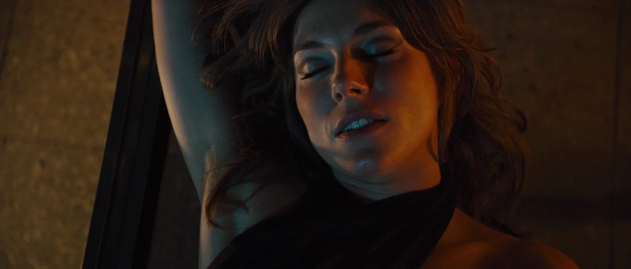 High-Rise (2015) movie still: closeup — A close-up view of a woman reclining in a darkened environment. She rests with her eyes closed while being…