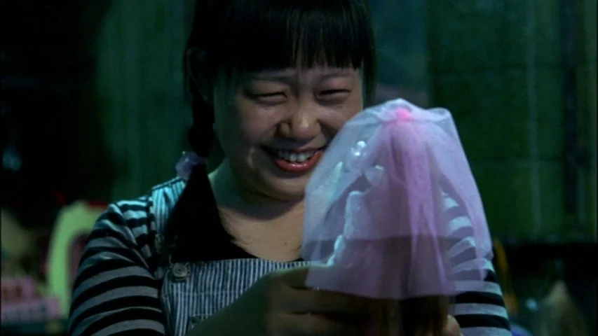 Save The Green Planet! (2003) movie still: closeup — A person in a dim room holds a toy doll. She gazes down at the doll's pink bridal veil with a…