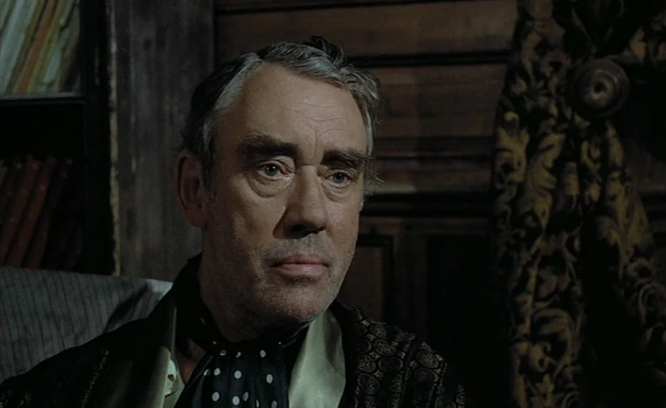 Lacombe, Lucien (1974) movie still: closeup — A dark, wood-paneled room containing bookshelves and heavy patterned curtains in the background. An…