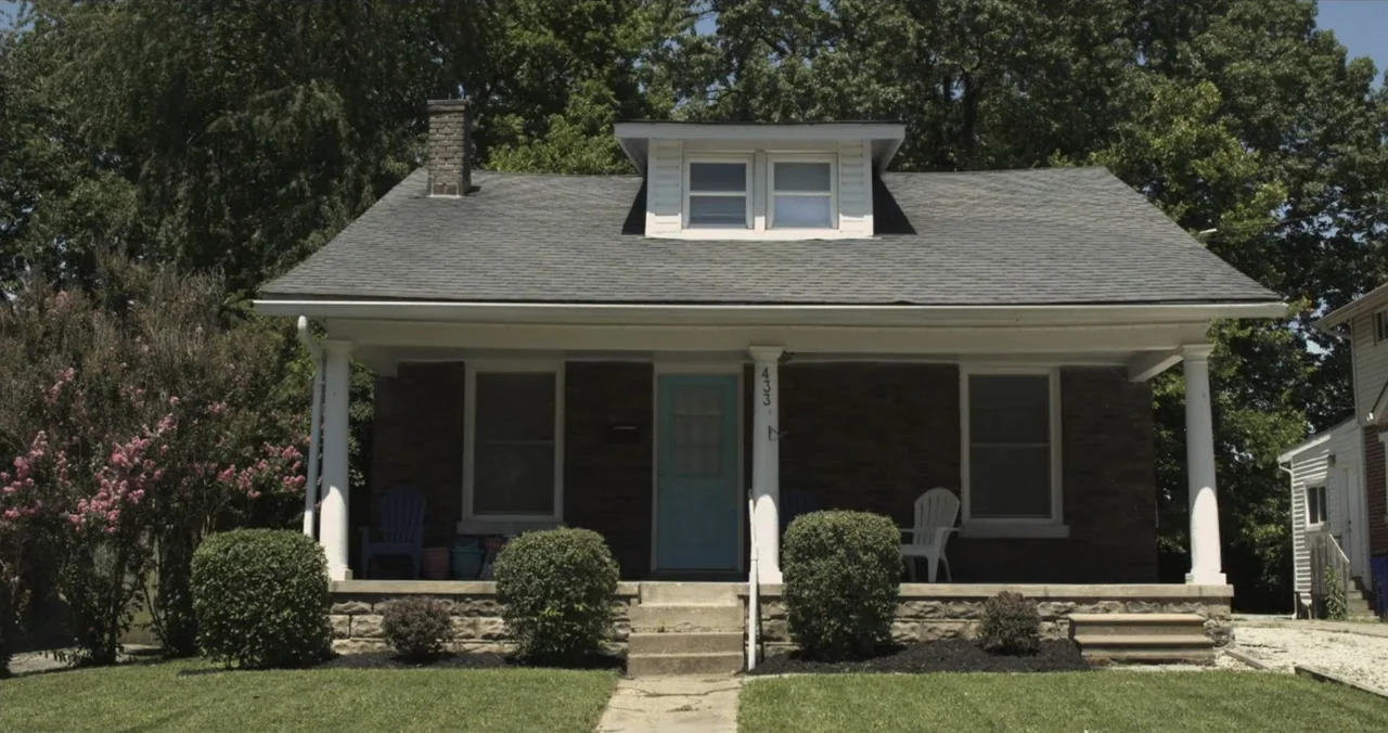 Faith, Love & Chocolate (2018) movie still: wide — A single-story brick residential house features a front porch and a blue door. The structure has…