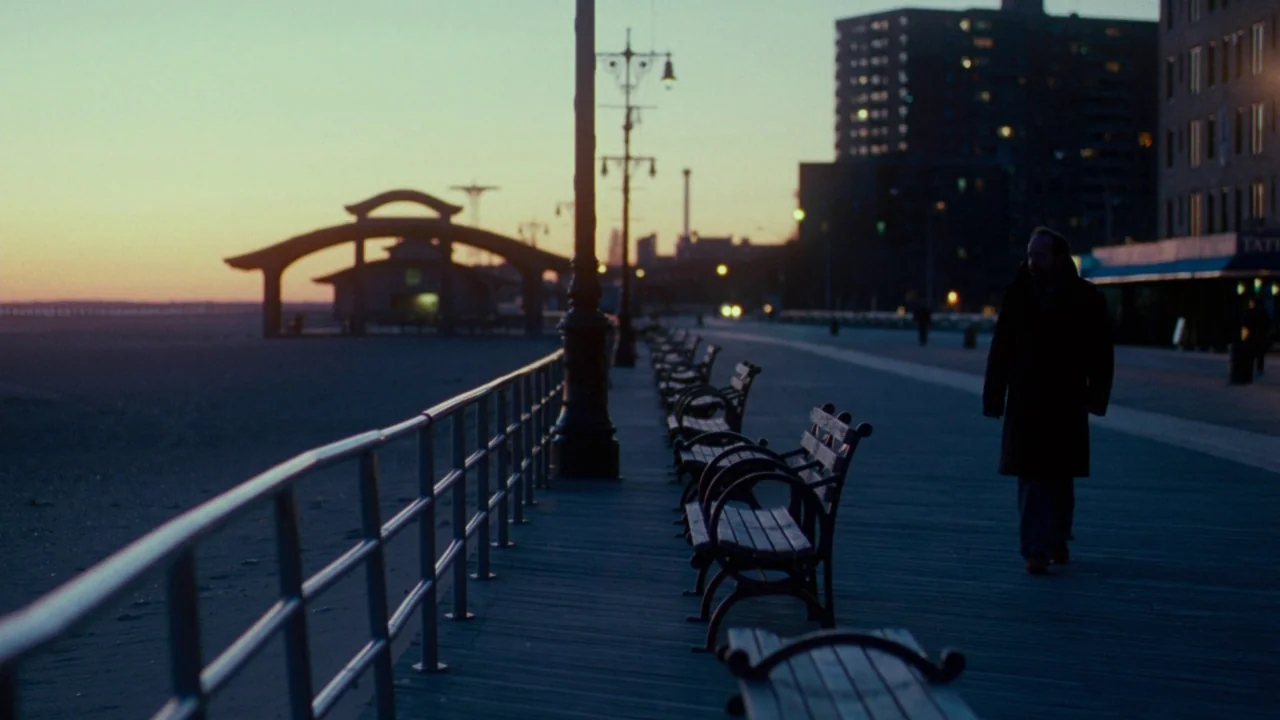 Cold Souls (2009) movie still: wide — A seaside boardwalk stretches toward a silhouetted structure during a calm sunset. A man walks away from the…