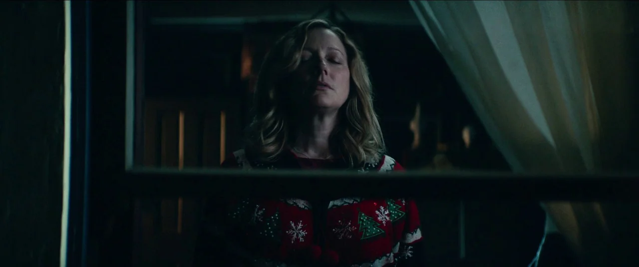 Halloween Kills (2021) movie still: medium — A dimly lit room with dark surroundings framed by a horizontal window pane. A woman with wavy hair…