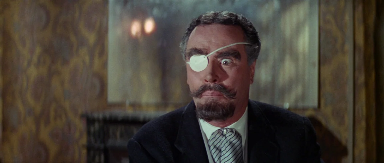 Irma La Douce (1963) movie still: closeup — A man stands in front of a patterned wallpaper with a blurred mirror reflection. He wears an eye patch…