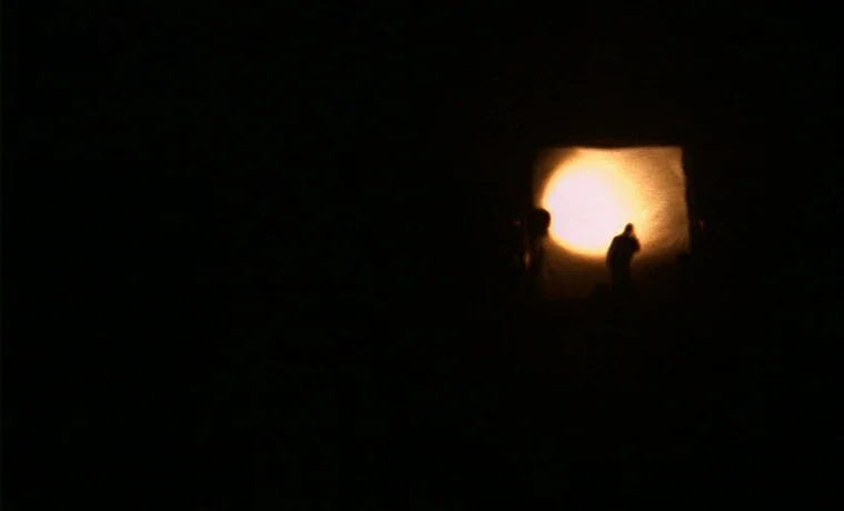 The Garden (1990) movie still: wide — A dark, empty space is occupied only by a single glowing circular light source. A solitary person stands in…