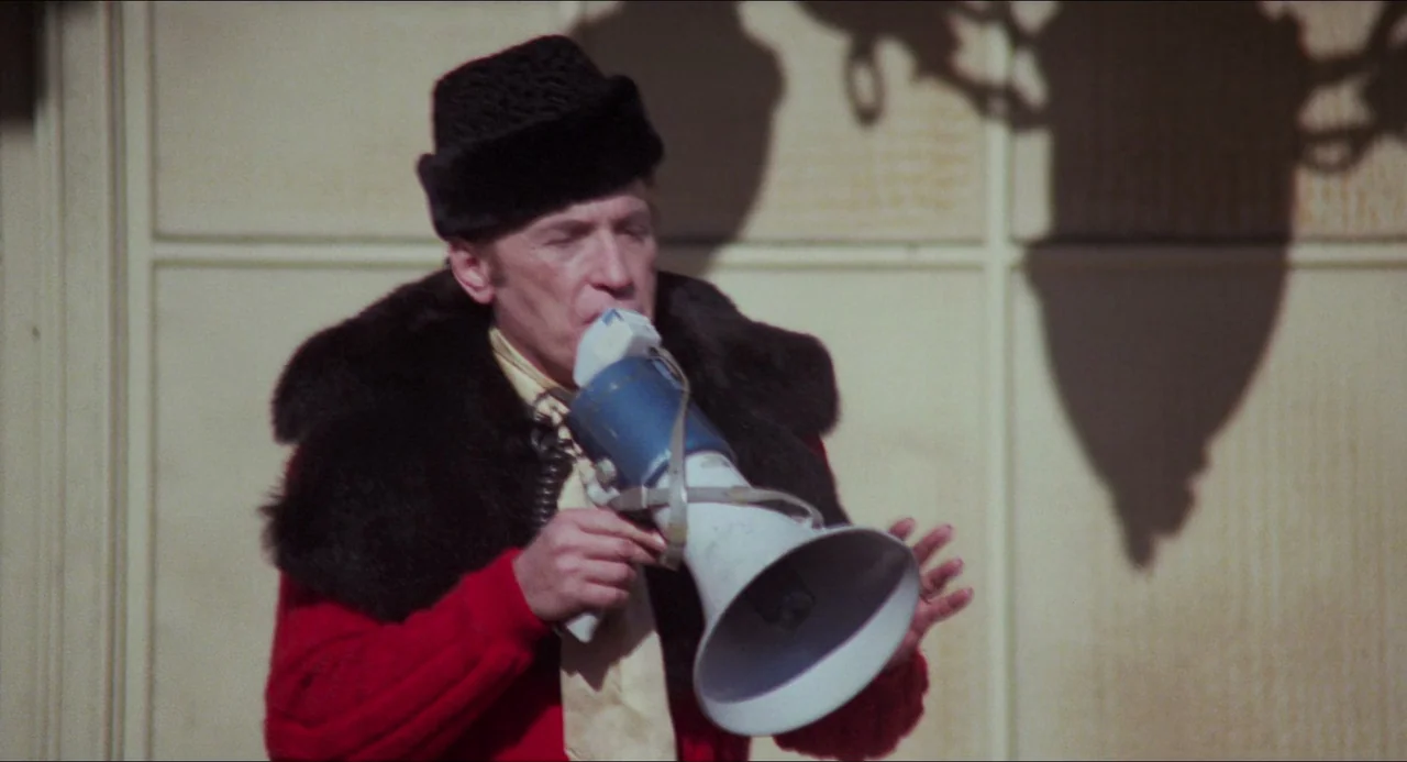 I Wanna Hold Your Hand (1978) movie still: medium — A man stands in front of a plain wall marked with large rectangular panels. He holds a blue and…