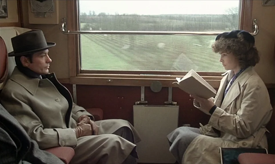 Mr. Klein (1976) movie still: medium — A 1940s train carriage cabin with wood paneling and red upholstery seats. A man sits facing a woman who is…