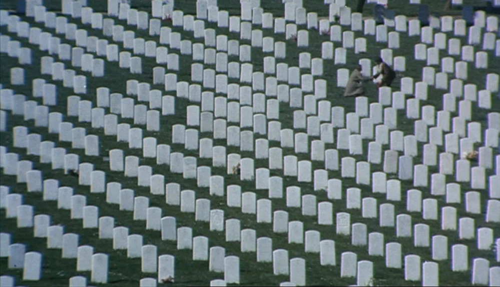 Harold and Maude (1971) movie still: wide — A vast military graveyard contains hundreds of uniform white headstones set in green grass. Two figures…