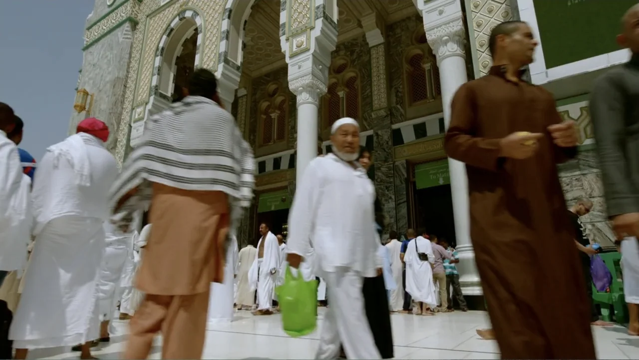 One Day in the Haram (2017) movie still: fullbody — A crowded marble plaza with ornate architectural arches in the background. Many individuals in…