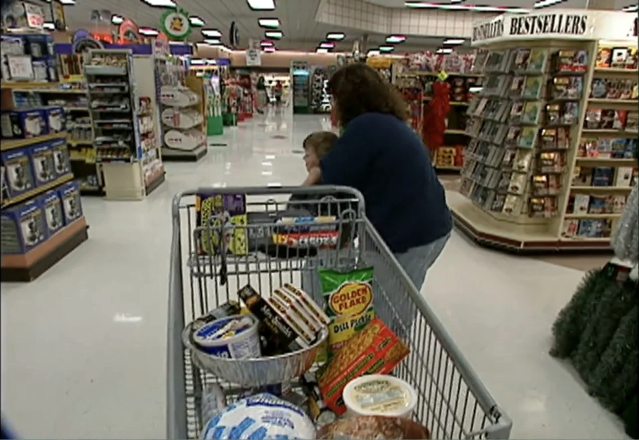 Broken Child (2000) movie still: medium — An aisle in a brightly lit grocery store contains shelves stocked with merchandise. A woman pushes a metal…