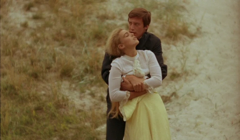 Elvira Madigan (1967) movie still: medium — A man and a woman stand together on a sandy, grass-covered dune. The man holds the woman closely from…