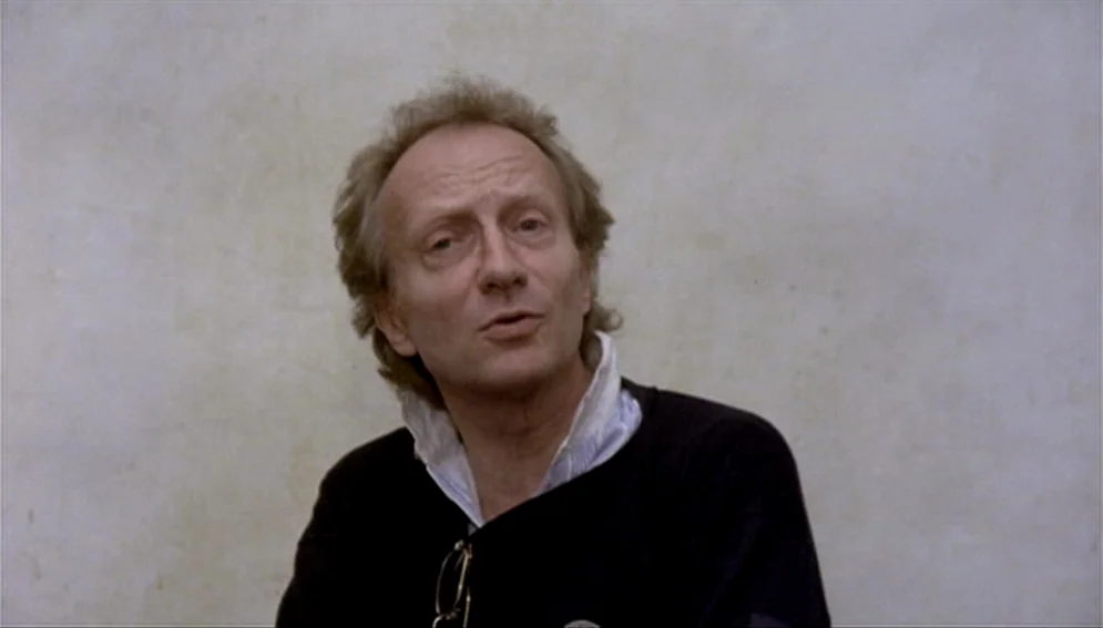 Orchestra Rehearsal (1978) movie still: medium — A man stands before a plain, light-colored wall with visible texture and subtle shading. He is…