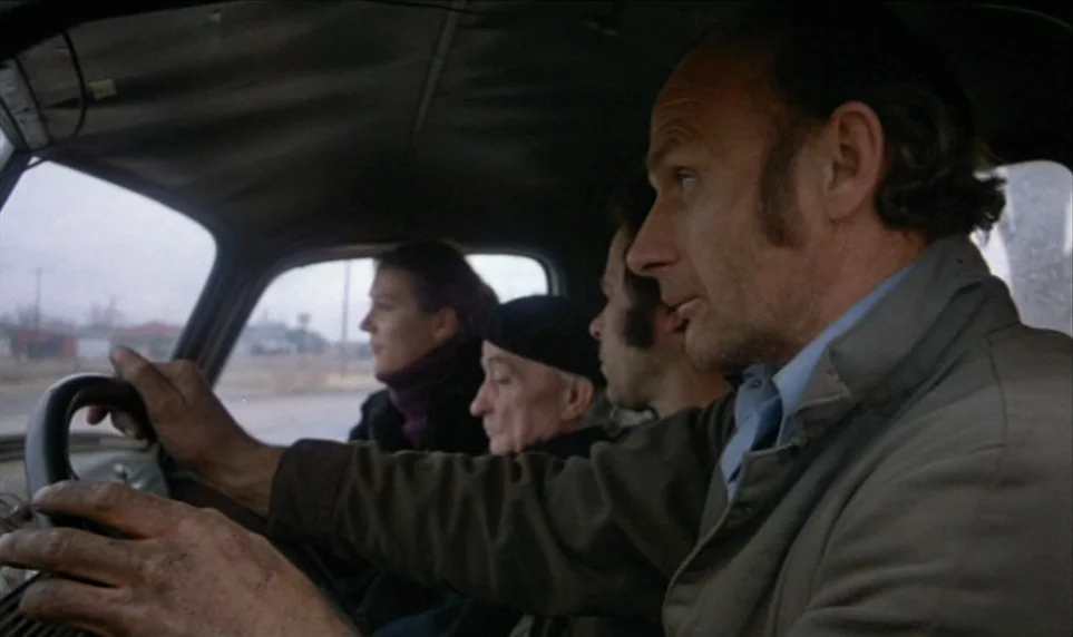 Stroszek (1977) movie still: medium — Four people travel inside a vintage car moving along a rural road. The driver stares ahead while the…