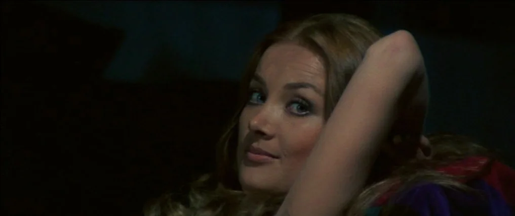 Don’t Torture A Duckling (1972) movie still: closeup — A dark, dimly lit indoor space with shadows obscuring the surroundings. A young woman with…