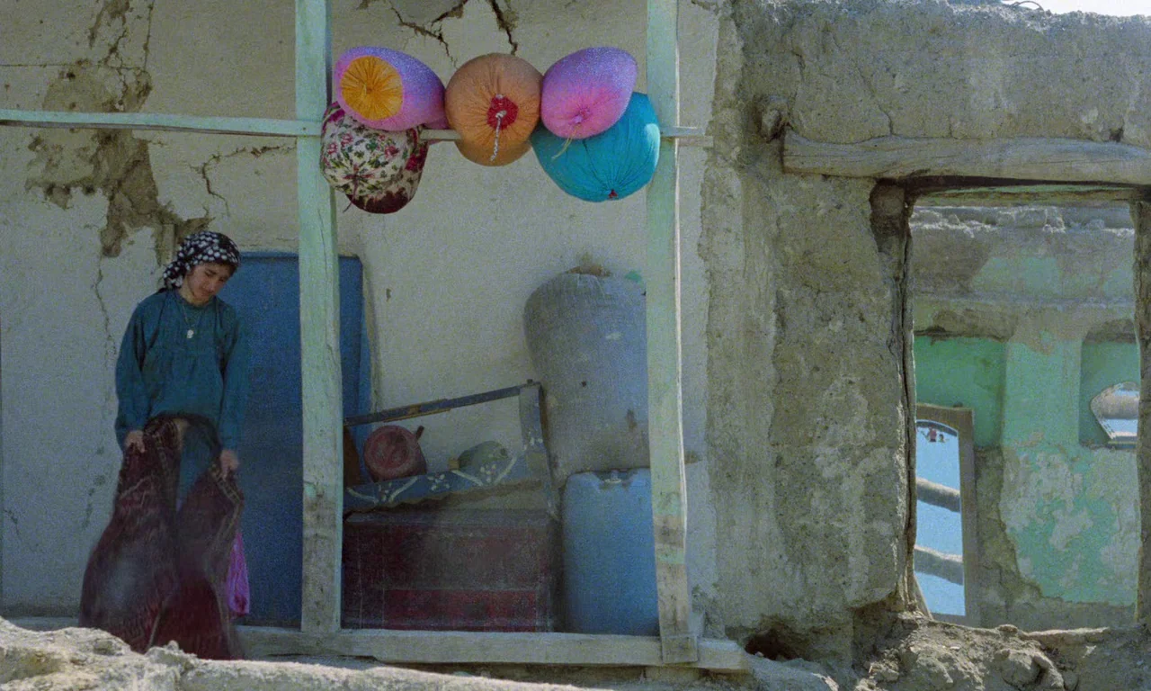 Life, and Nothing More (1992) movie still: medium — A crumbling adobe structure features a dirt foreground and an open doorway reveal. A young woman…