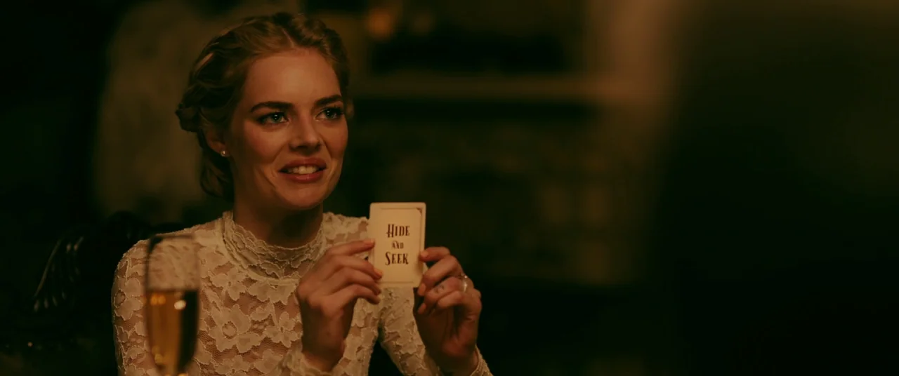 Ready or Not (2019) movie still: medium — A dimly lit room with a person dressed in white lace clothing. The woman holds a small rectangular card…