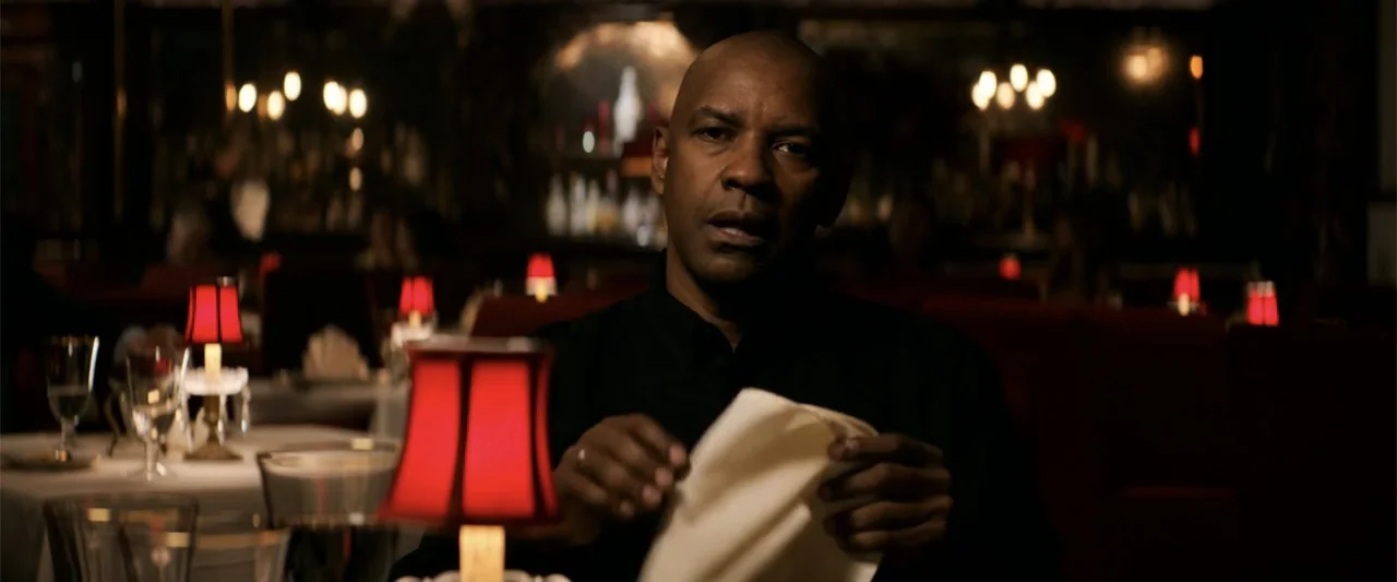 The Equalizer (2014) movie still: medium — A dimly lit upscale dining area features red table lamps atop white tablecloths. A man wearing a black…