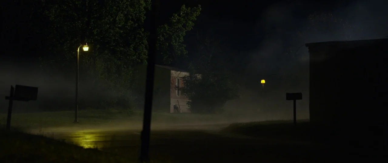 The Strangers: Prey at Night (2018) movie still: establishing — A dark residential street at night is obscured by a dense layer of fog. Two…