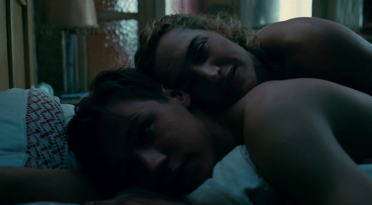 The Reader (2008) movie still: closeup — Two individuals lie close together in a dim, shadowed bedroom at night. They rest their heads side-by-side…