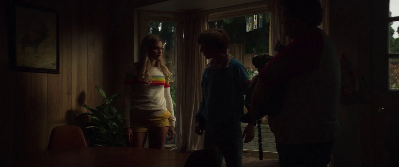 Summer of 84 (2018) movie still: medium — A 1980s home interior features wood-paneled walls and a framed print of a deer. Two teenagers and an adult…