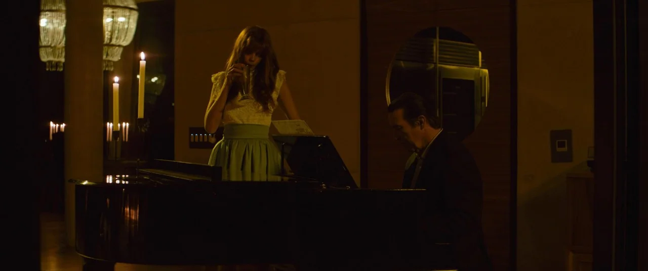 Elizabeth Harvest movie still: medium — A dimly lit room features a grand piano illuminated by several lit candles. A woman holds a glass while a…