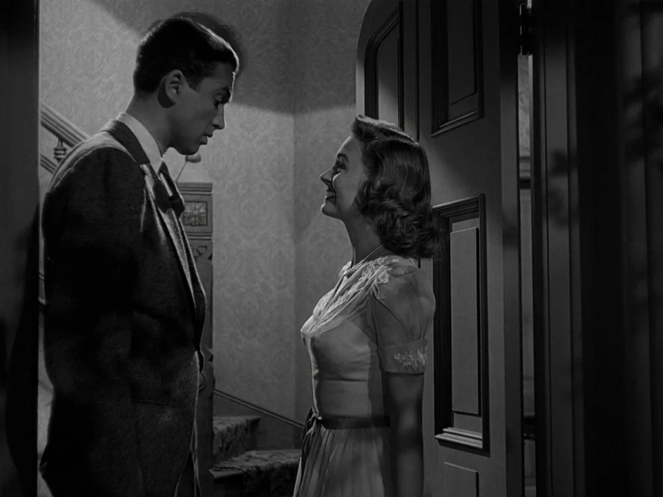 It’s A Wonderful Life (1946) movie still: medium — A dimly lit indoor foyer features patterned wallpaper and a prominent wooden arched door. A man…