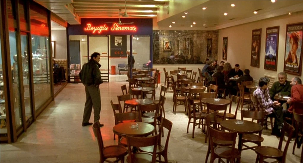 Uzak (2002) movie still: wide — A spacious cafe entrance with marble floors and dark wood furniture in an open lobby. A man in a leather jacket…