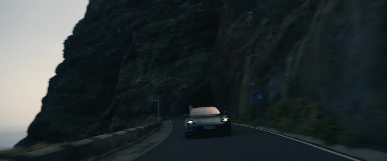 Den of Thieves 2: Pantera (2025) movie still: wide — A modern car travels on a narrow winding coastal road beneath a massive rock face. The vehicle…